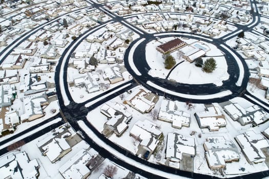 Aerial image showcasing a snow-blanketed suburban neighborhood. The circular road layout and uniform houses present a serene winter scene from above, highlighting the beauty of snowy landscapes.