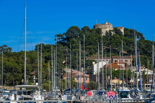 France, Porquerolles, June 9, 2024: Boats in the harbor of Porquerolles Island, and Fort Sainte Agathe in the distance, Var, Provence, France. High quality photo