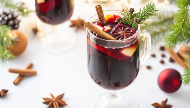 Glass of mulled wine is surrounded by christmas decorations and spices on a white background