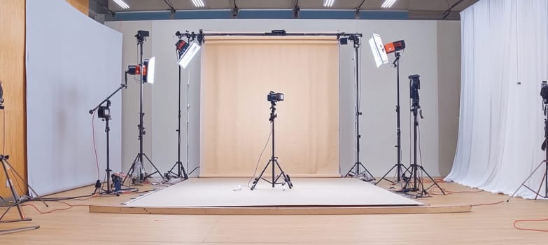 Several studio lights are illuminating a white and a beige backdrop in an empty photo studio