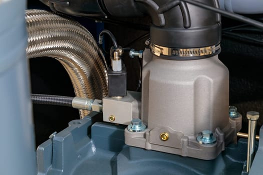 Close-up of an industrial air compressor pump featuring a flexible metal hose, valves, and various mechanical components