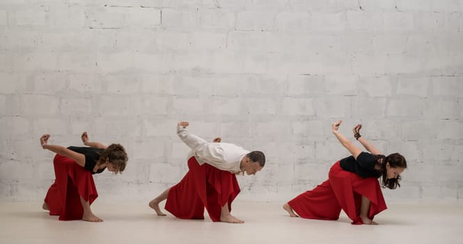 Two women and their male trainer doing yoga exercises view against brick wall