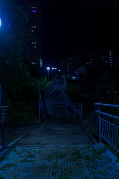 An urban stairway illuminated by streetlights leads up between apartment buildings at night. The quiet and empty scene captures a peaceful residential area with no people visible