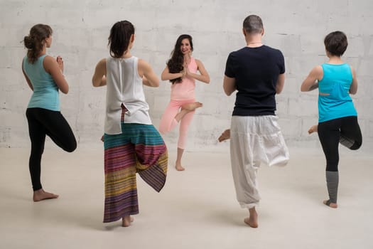 Group of women and their male trainer in sportswear doing yoga view against brick wall