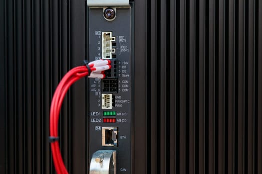 Red cable connecting to input output module of a programmable logic controller with visible leds and communication ports