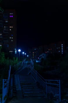An urban stairway illuminated by streetlights leads up between apartment buildings at night. The quiet and empty scene captures a peaceful residential area with no people visible