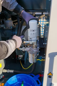 Close-up of a technician's hands replacing an oil filter during maintenance on an industrial air compressor