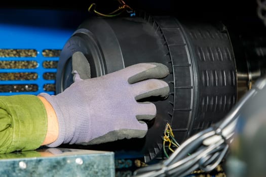 Close-up of a technician's gloved hand working on an air filter within a piece of industrial machinery