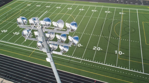 Aerial photograph of a football field showing yard lines and stadium lighting, showcasing a well-maintained sports facility. Ideal for school sports and athletic event designs.