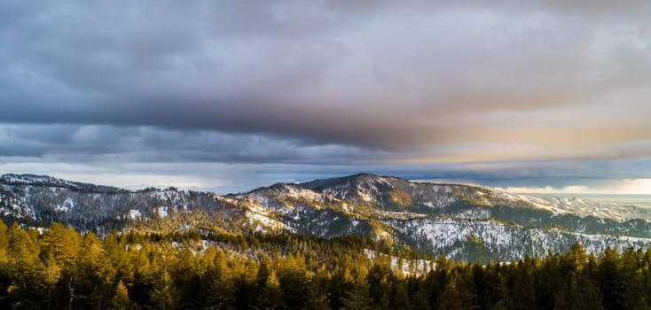 Scenic view of a snow-capped mountain range under a dramatic cloudy sky, illuminated by the warm glow of sunset. Perfect for nature lovers and outdoor enthusiasts.