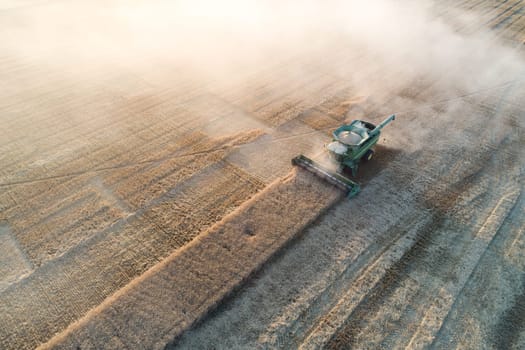 Aerial shot of a combine harvester operating in a vast wheat field, producing dust clouds. Captures the essence of agricultural harvest and rural farming landscapes
