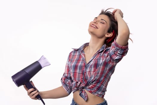 A confident young woman is blowdrying her hair, showcasing the latest modern haircare trends and techniques
