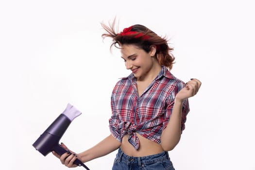 A vibrant young woman is playfully using a hair dryer, showcasing her fun attitude and stylish, chic look