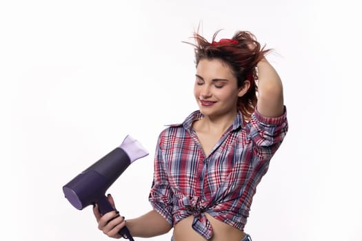 A young woman joyfully dries her hair with a hairdryer, showcasing a fun and trendy vibe in her style