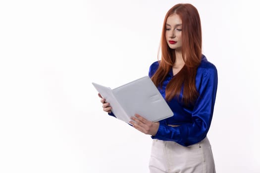 A young woman in a chic blue blouse is absorbed in reading a book, showcasing her modern and stylish look