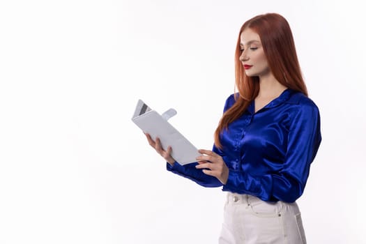 A young woman wearing a stylish blue satin shirt is deeply engrossed in reviewing a document with confidence and focus