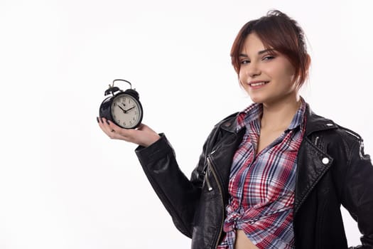 A trendy young woman confidently poses with an alarm clock, showcasing her stylish outfit and vibrant demeanor