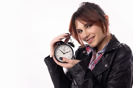 A stylish young woman smiles broadly while confidently holding an alarm clock, showing a joyful sense of urgency