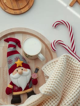 The image presents a festive scene set on a white surface. Dominating the center is a charming gnome figurine, adorned in a vibrant red and gold outfit, complete with a matching hat and a white beard. The gnome is holding a white mug, which is filled with a white liquid, possibly milk. To the right of the gnome, there are two candy canes, one red and one white, adding a pop of color to the scene. The background is blurred, drawing focus to the gnome and its surroundings.