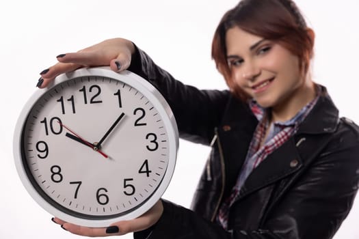 A young woman is happily smiling while holding a large clock, which is perfect for themes related to time management