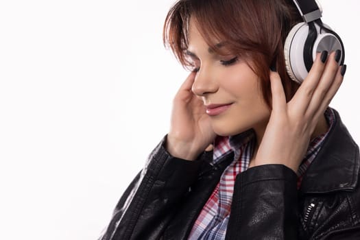 A young woman completely immersed in her music, wearing stylish headphones and a trendy leather jacket