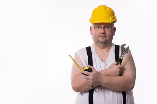 A construction worker wearing a yellow hard hat is holding tools and is prepared for various construction tasks ahead