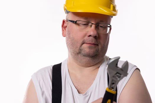 A diligent and focused construction worker carefully evaluates an adjustable wrench while wearing proper safety gear