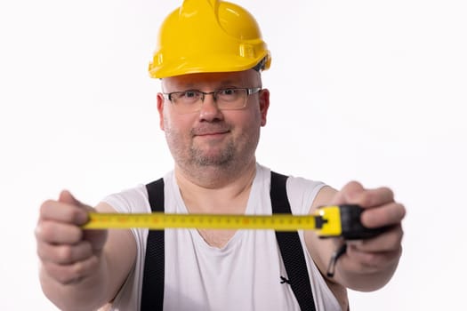 A construction worker in a yellow hard hat measures using a tape measure, showcasing tools of the trade.