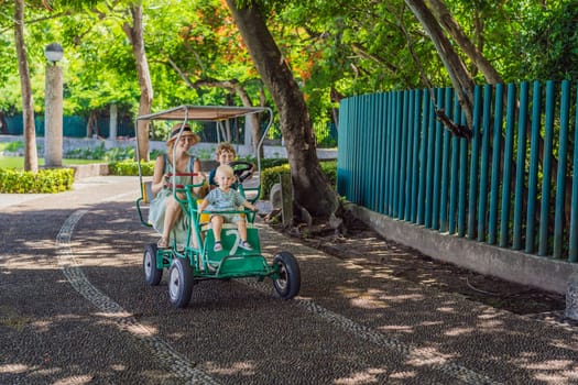 Mother tourist with her toddler and teenage sons riding an authentic Mexican pedal car in a park in Mexico. Family adventure and travel with kids concept.
