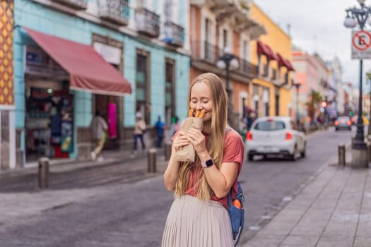 Female tourist eating churros on a colonial street in Puebla, Mexico. Cultural experience, local cuisine, and street food exploration concept.