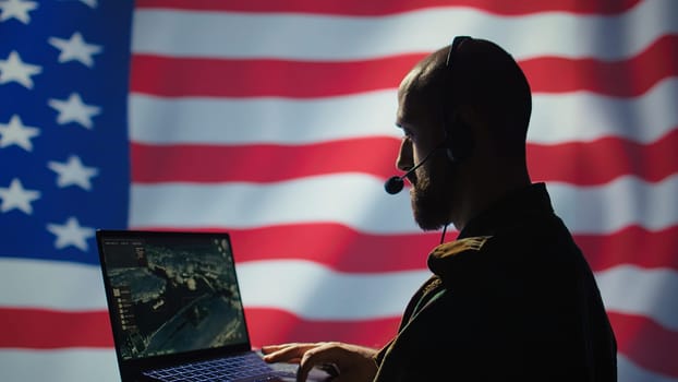 US Air Force dispatcher looking at surveillance transmission on device, relaying data to ground soldiers from control room using headset, isolated over United States flag background, camera B