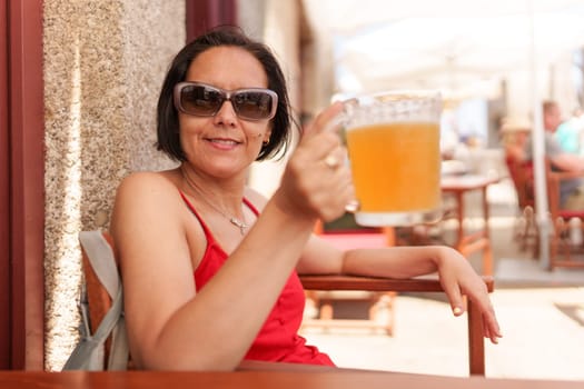 Smiling woman in sunglasses drinking a mug of beer in summer