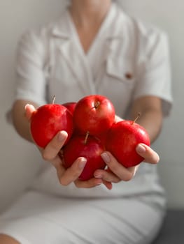 Woman in white dress holding fresh red apples in hands.