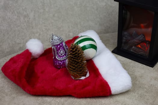 Tree cone next to Christmas toys. Decorations for New Year tree lie on red cap next to mini fireplace to create festive atmosphere, toys for happy new year and Christmas