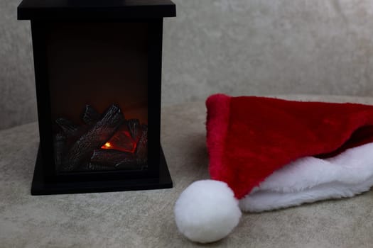 Portable fireplace for decorating interior of home for New Year against background of red cap, attributes of Christmas and New Year on light background, creating festive atmosphere