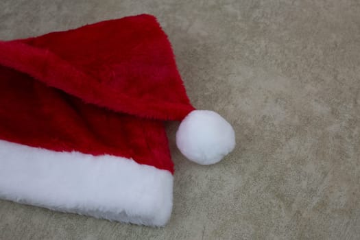 Furry red cap for New Year lies on light background with text place, fluffy hat with pompom for Christmas on plain background, concept of New Year holiday, must have Christmas attribute