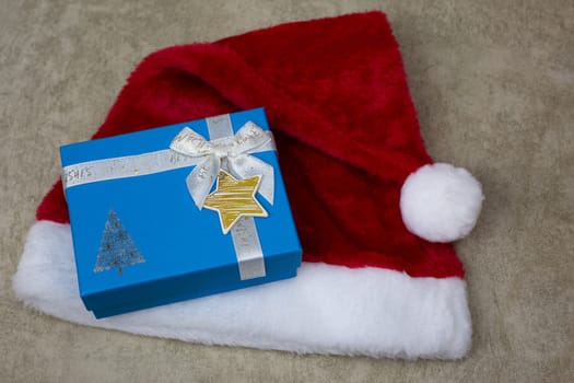 Fluffy red hat with pompom for New Year lies with blue gift box in Christmas, gift in box on background of New Year cap, winter holiday attributes