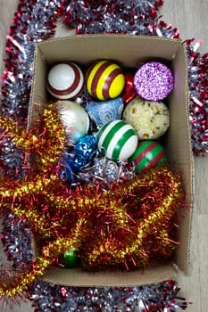 Vertical photography of tinsel and Christmas tree decorations in box. Start decorating house and Christmas tree for New Year and Christmas, storing Christmas tree decorations in cardboard box
