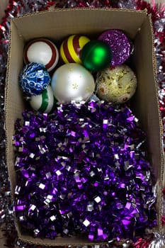 Bright tinsel and New Year balls for Christmas tree in cardboard box, top view, storing New Year's toys for home decoration for New Year