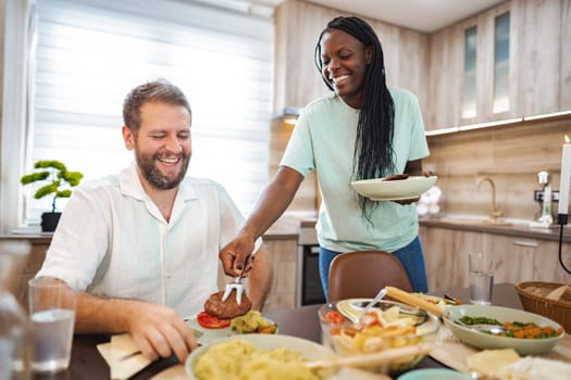 A woman serves a hearty dish to a smiling man during dinner time.
