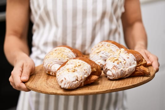 female baker holding wooden tray with freshly baked crispy golden croissants