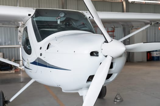 Close-up of a small white airplane with a propeller, parked in a hangar, showcasing its cockpit and wings.