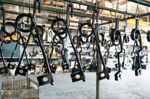 Close-up of black-coated metal parts hanging in a factory or workshop, ready for processing or assembly.