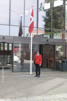 aalborg,denmark,03-09-2024: den gamly by ,A guard in a red uniform stands by the Danish flag in front of a modern building. The scene represents tradition, nationalism, and duty.