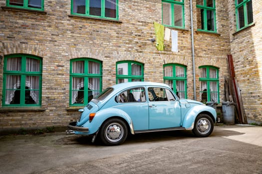 arhus,denmark,03-09-2024:A vintage blue vw car is parked in front of an old brick building with green window frames, creating a nostalgic atmosphere. The scene captures the charm of urban vintage aesthetics