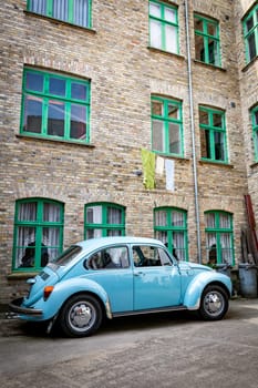 arhus,denmark,03-09-2024:A vintage blue vw car is parked in front of an old brick building with green window frames, creating a nostalgic atmosphere. The scene captures the charm of urban vintage aesthetics