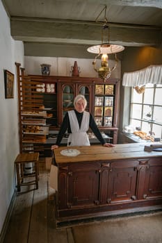 arhus,denmark,03-09-2024:A baker in a vintage bakery shop, showcasing a historical setting with wooden shelves and classic decor, conveys nostalgia and tradition. Well-lit atmosphere highlights a warm, inviting environment.