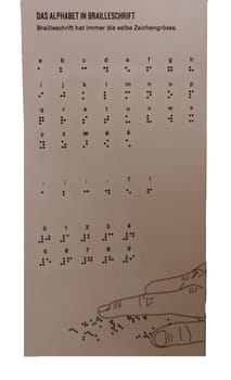 Educational chart displaying the Braille alphabet with descriptions in multiple languages, emphasizing its consistent size. Features a stylized hand reading Braille dots, promoting inclusivity and accessibility.
