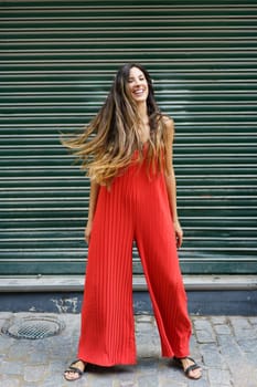 A cheerful and vibrant woman dressed in a stylish red jumpsuit poses playfully and confidently against a textured green backdrop, beautifully showcasing her love for fashion and selfexpression