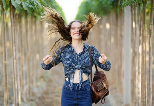 A cheerful young woman stands amidst tall, lush plants, joyfully tossing her hair with a radiant smile, beautifully capturing a moment of pure happiness and delight in nature all around her